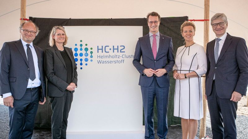 Professor Wasserscheid, BMBF-Staatssekretärin Pirscher, Ministerpräsident Wüst, MKW-Ministerin Brandes und Professor Marquardt vor dem Logo des Helmholtz-Clusters Wasserstoff. 
