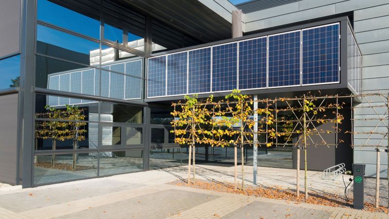 Foto eines Gebäudes mit Fassaden-PV und einer E-Ladesäule im Vordergrund