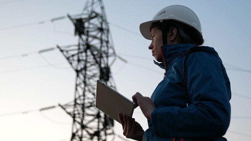 Eine Frau mit Tablet in der Hand steht vor einem Strommast. 