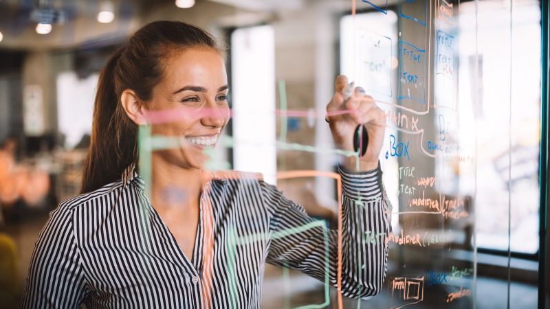 Eine Frau notiert Überlegungen auf einer durchsichtigen Glas-Notizwand