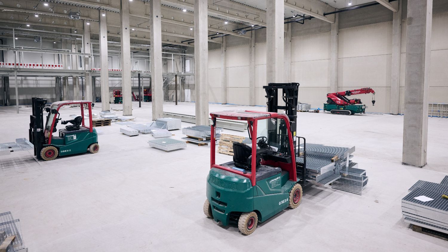 Blick in ein FFB-PreFab-Gebäude: In der hohen Halle mit Betonwänden und -säulen stehen Gabelstapler und warten auf ihren Einsatz. 