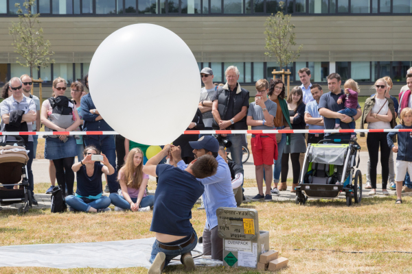 Zwei Wissenschaftler treffen Vorbereitungen, um einen Wetterballon steigen zu lassen. Sie werden gespannt von den umstehenden Besucherinnen und Besuchern beobachtet.