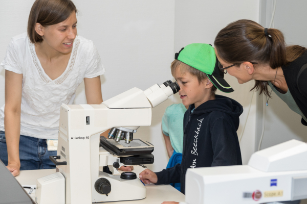 Eine Wissenschaftlerin begeistert Kinder für den Blick ins Mikroskop.