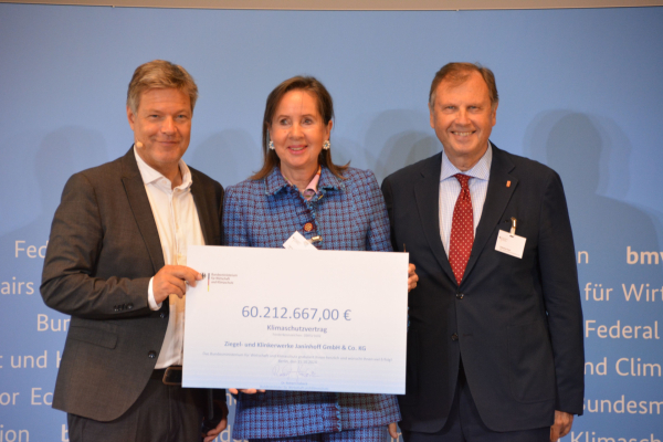 Die Vertreter der Firma Ziegel- und Klinkerwerke Janinhoff GmbH & Co. KG und Robert Habeck stehen nebeneinander und halten ein großes Plakat als Symbol für den Klimaschutzvertrag vor sich.